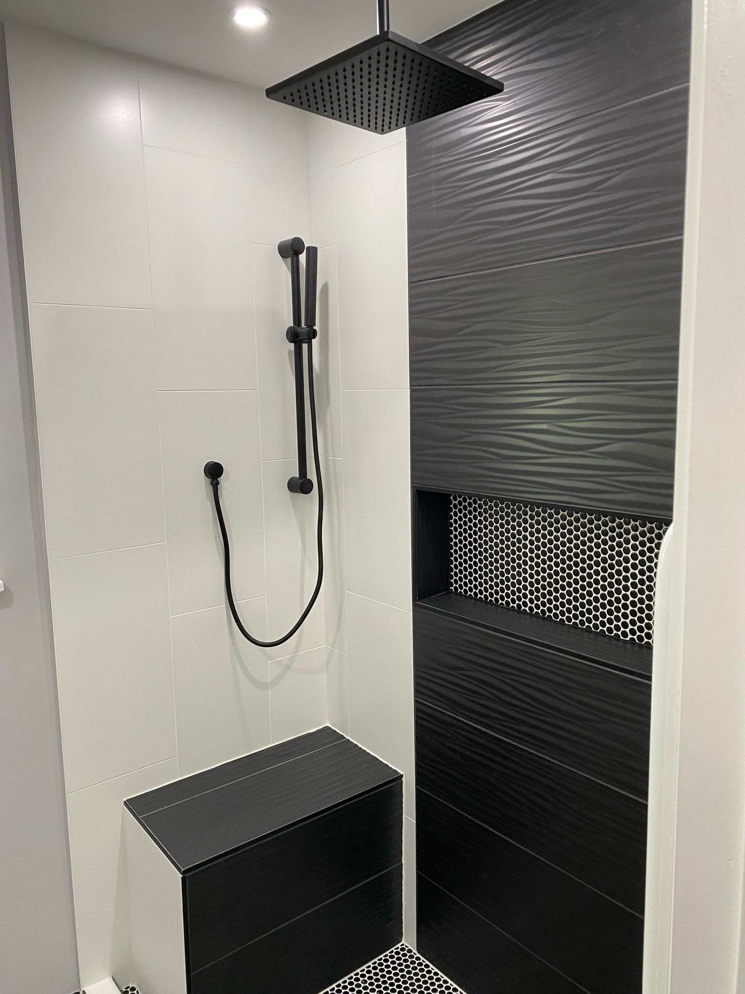 Modern shower stall with black fixtures, white tile, and a built-in bench.
