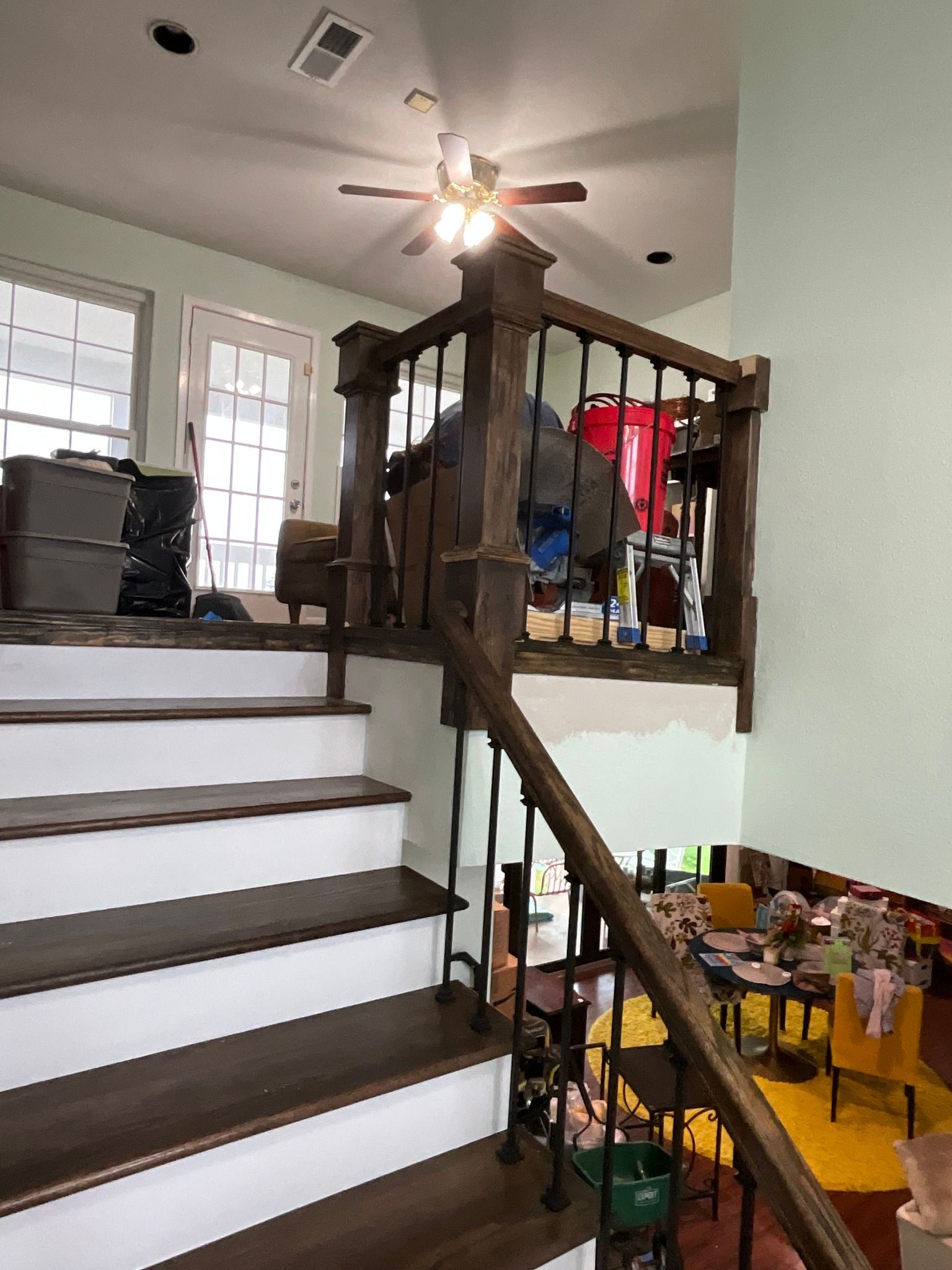 Indoor staircase with dark wood railing, white steps, and a bright living area below with toys and furniture.