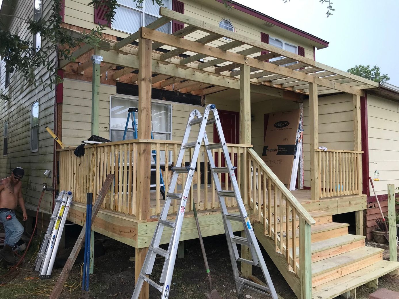 Partially built wooden porch with stairs, ladders, and construction materials beside a house