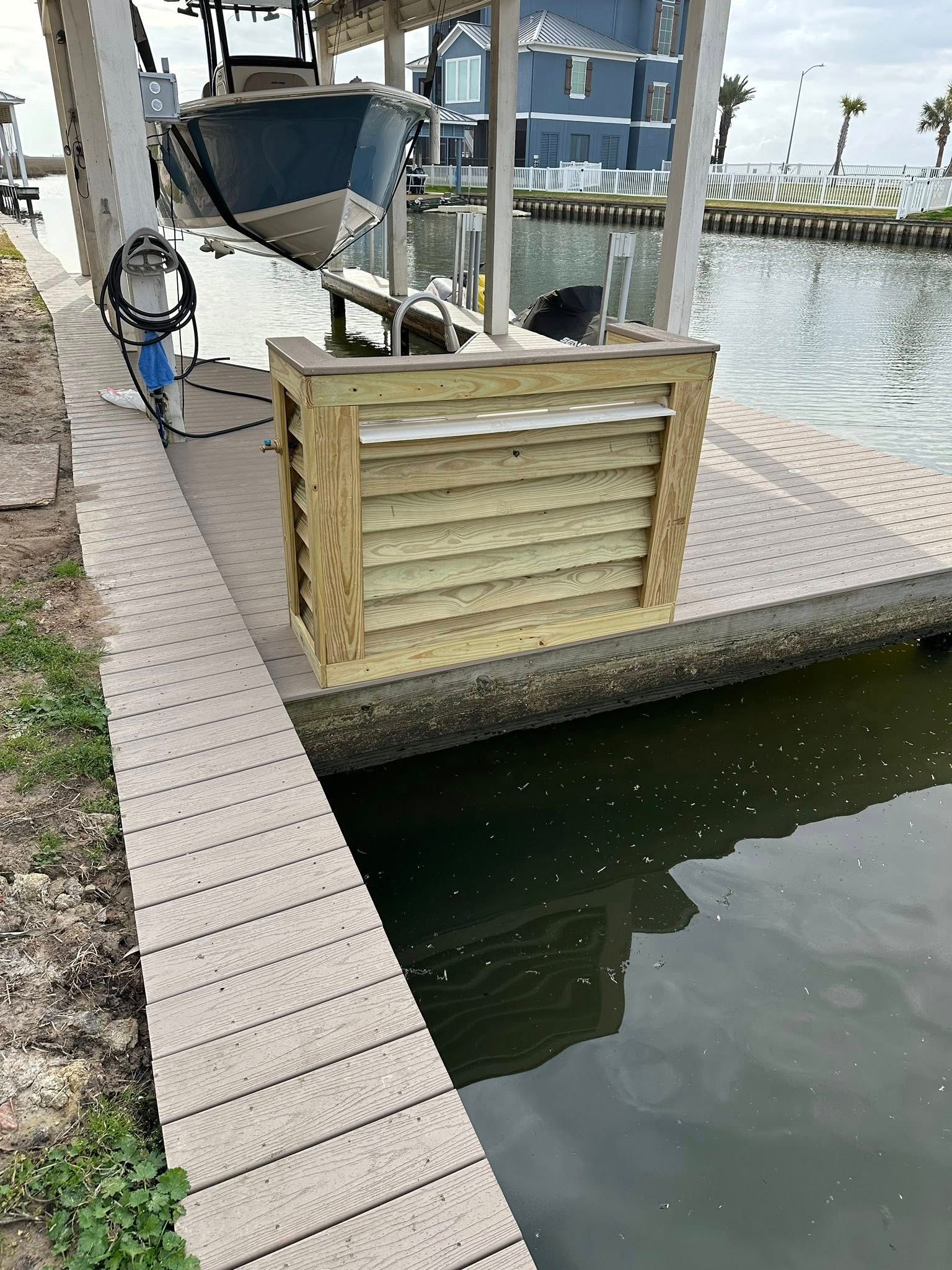 Canal-side dock with a boat lift, wooden barrier, and calm water beside a paved walkway