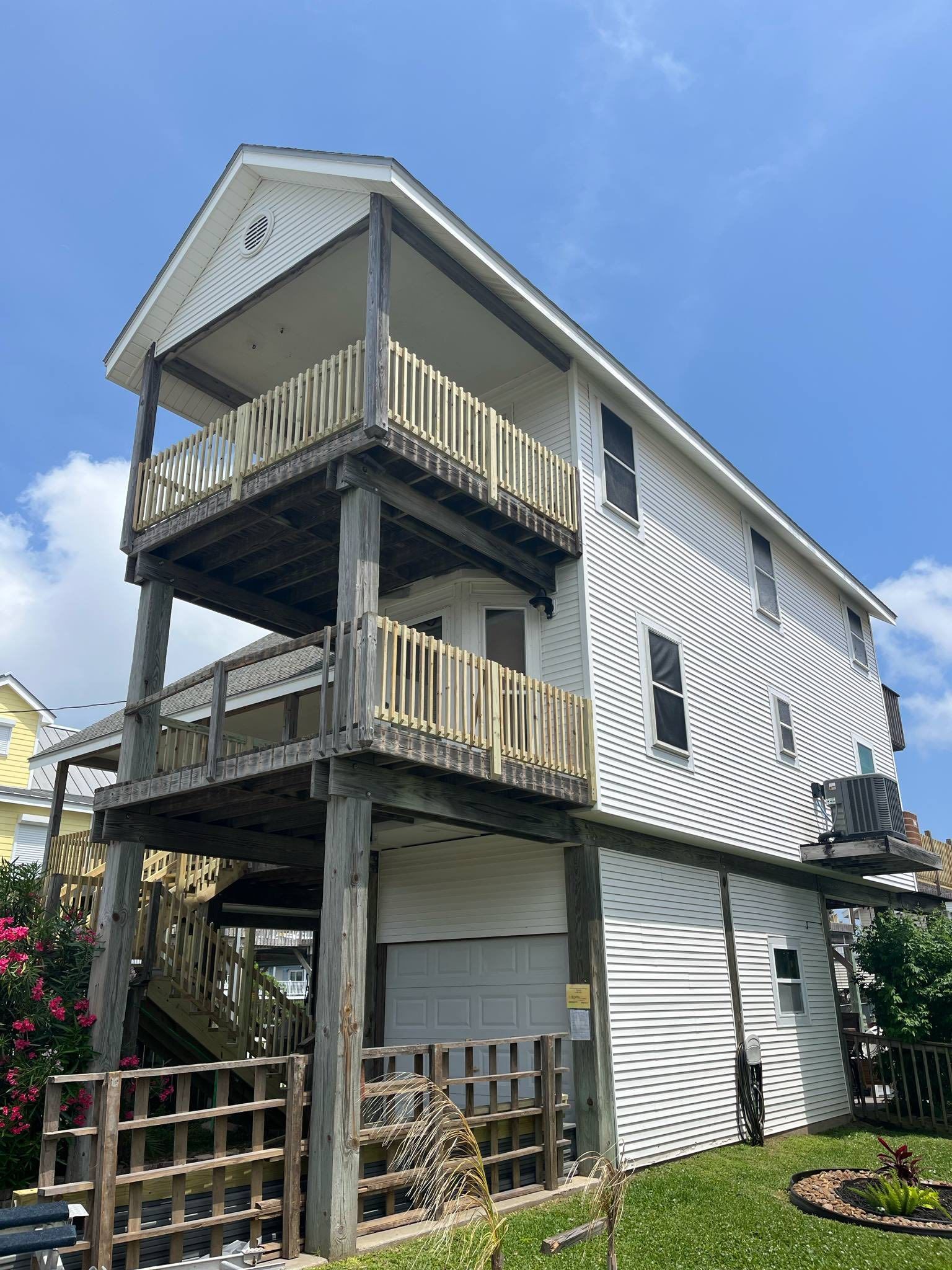 Three-story white house with stacked wooden balconies and stairs under a blue sky