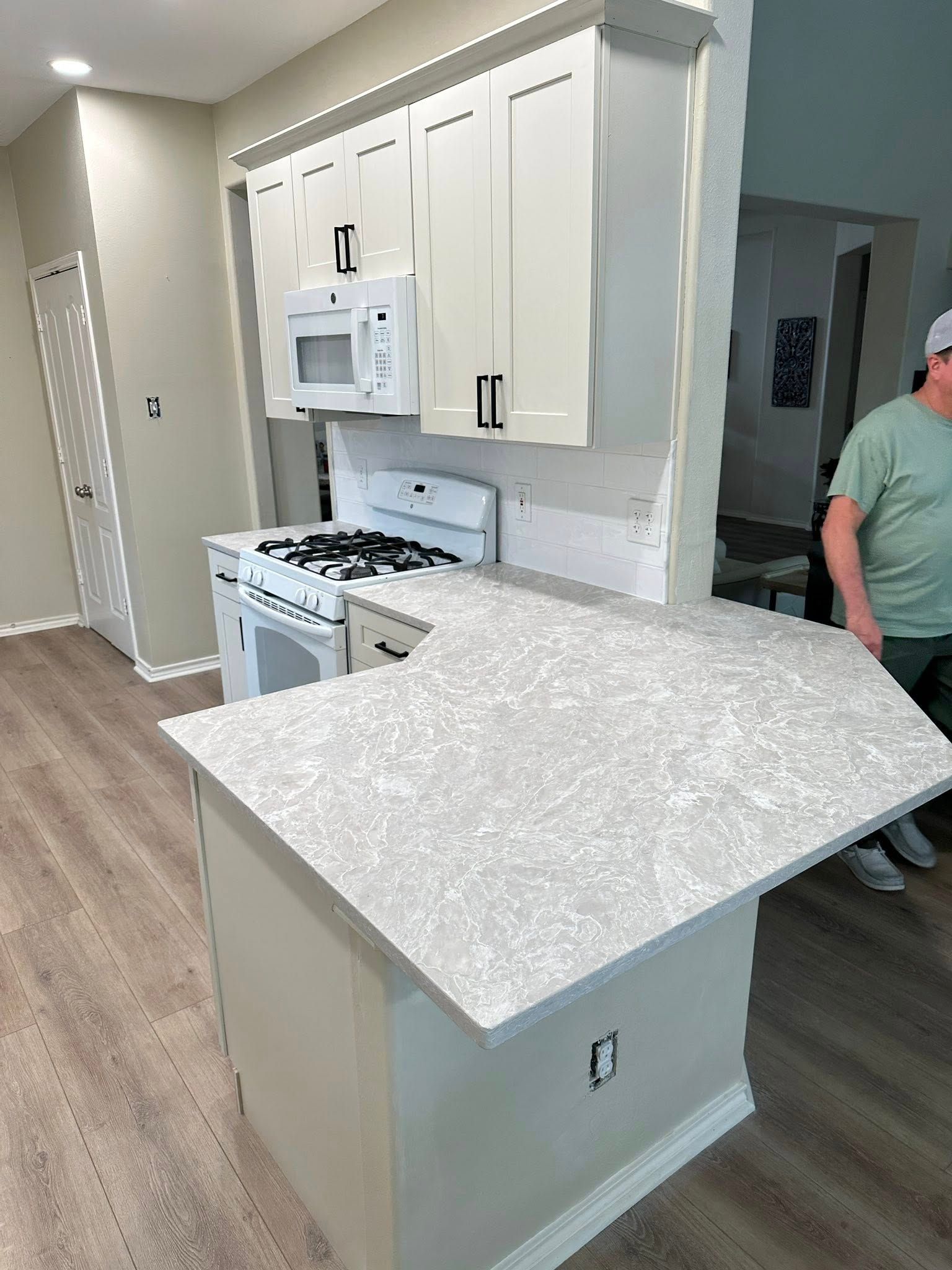 Modern kitchen with white cabinets, stove, microwave, and a gray speckled island counter