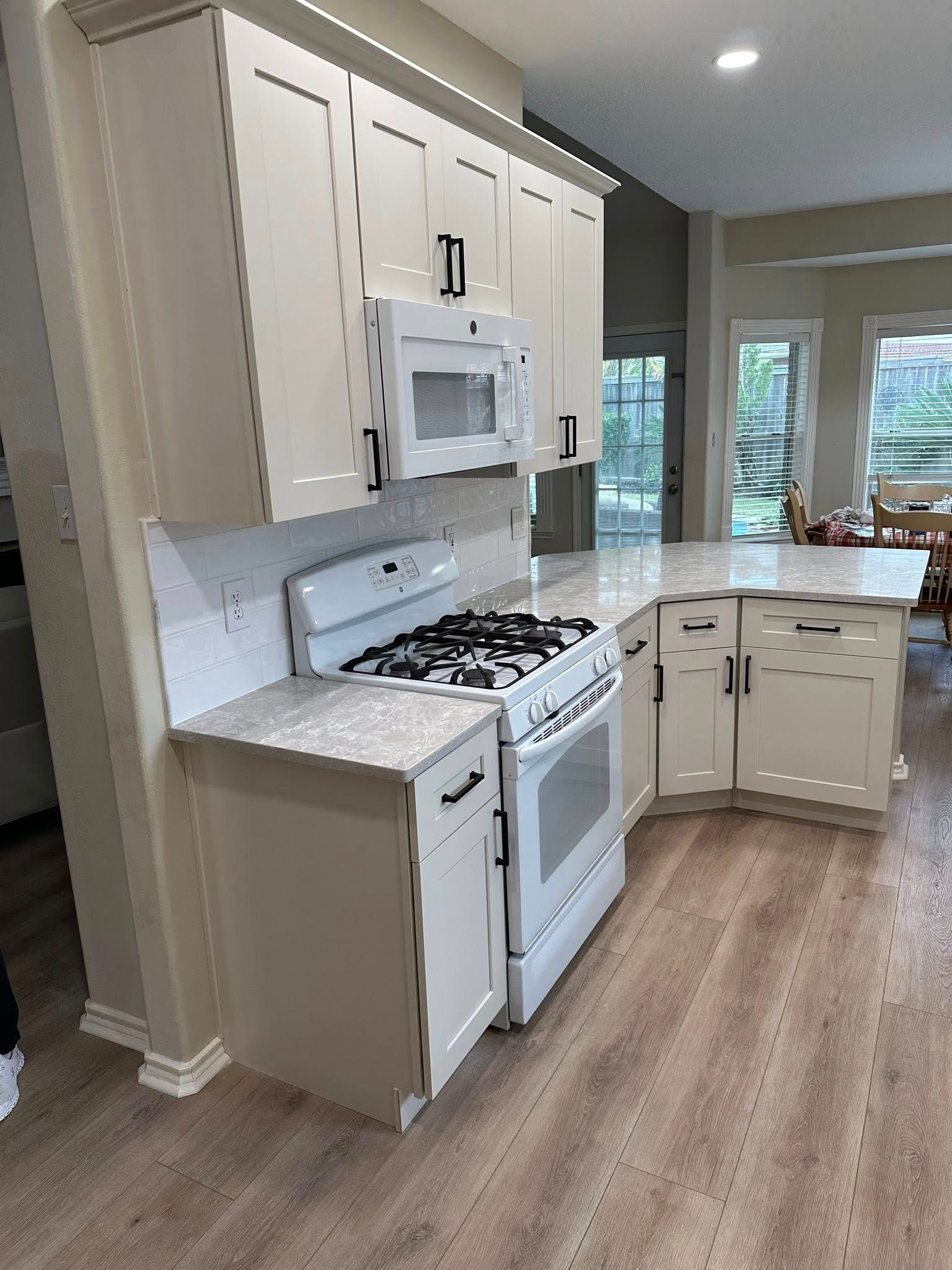 Bright kitchen with white cabinets, white appliances, and a wood-look floor near a windowed dining area