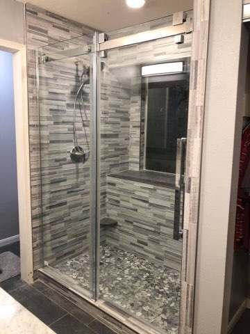 Glass walk-in shower with gray tile walls and a chrome showerhead and doors