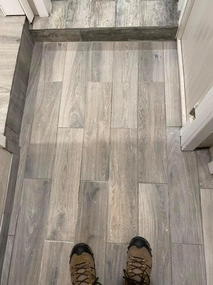 View from standing at the top of stairs onto wood-look flooring, with a person’s shoes visible at bottom.