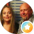 Two people posing closely, with a circular orange-and-white badge overlay in the corner
