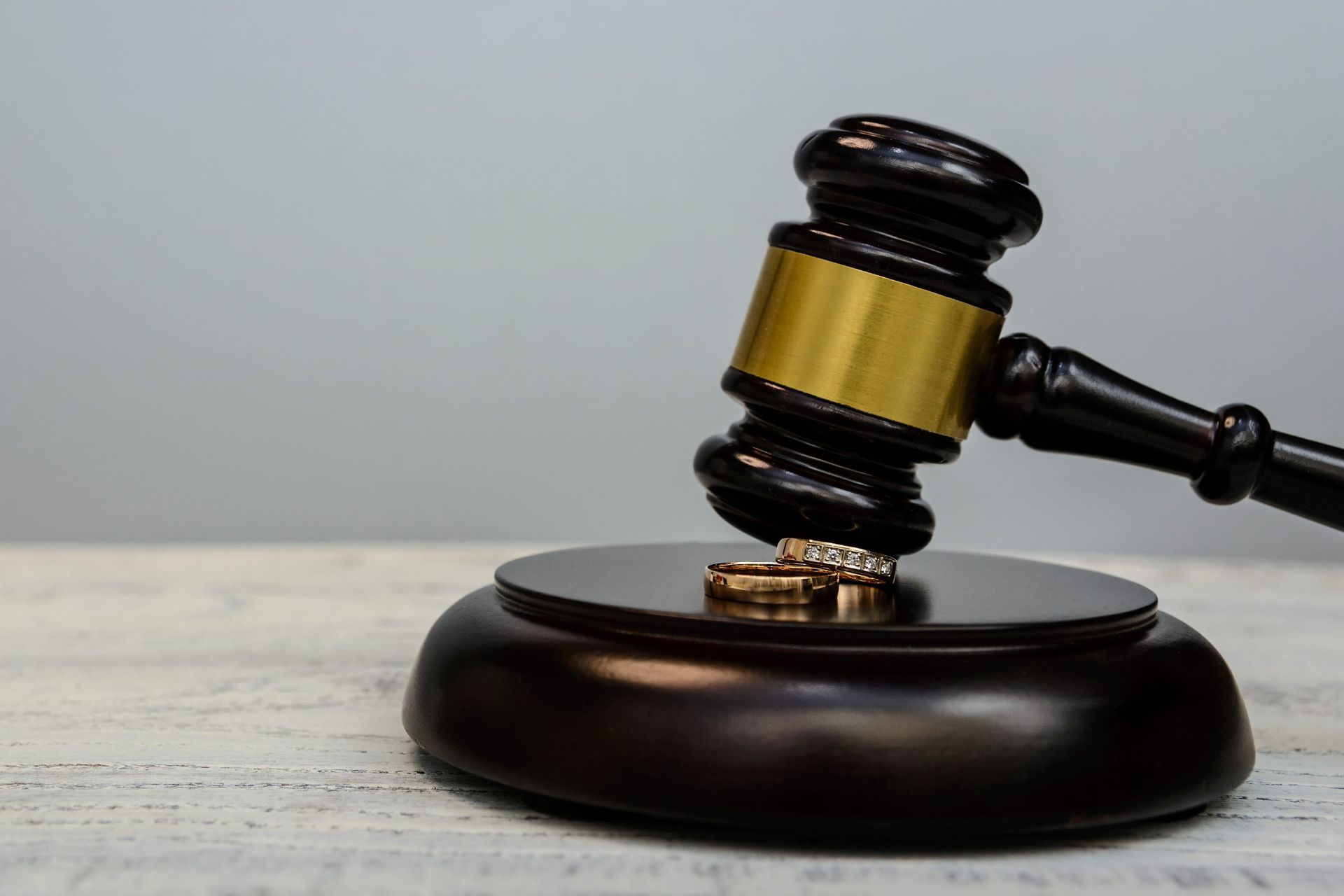 A wooden gavel resting on its sounding block over two wedding rings on a light wooden surface.