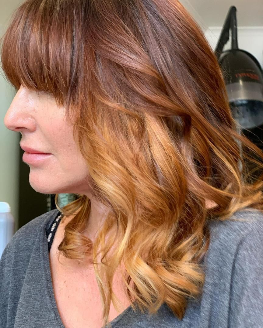 A Woman With Long Brown Hair and Bangs is Wearing a Gray Shirt — Energy Hair Co in Noosa Heads, QLD