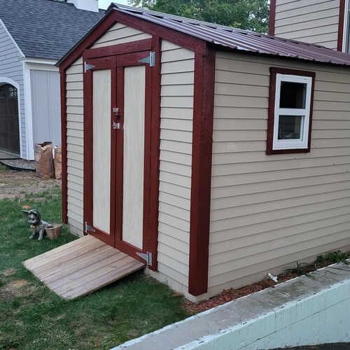 A shed with a ramp and a window in the backyard of a house