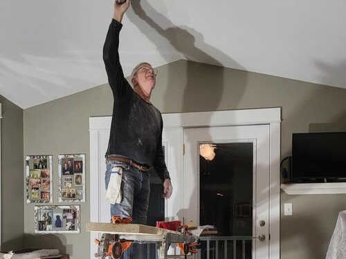 A man is standing on a ladder in a room working on a ceiling A man is standing on a ladder in a room working on a ceiling