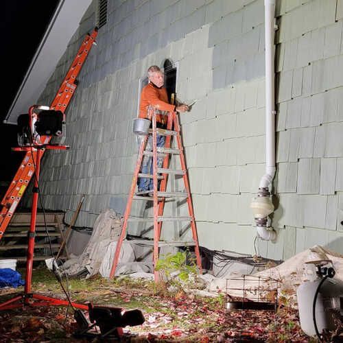 Dan is standing on a ladder painting the side of a house