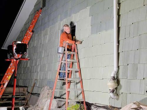 A man is standing on a ladder painting a house A man is standing on a ladder painting a house