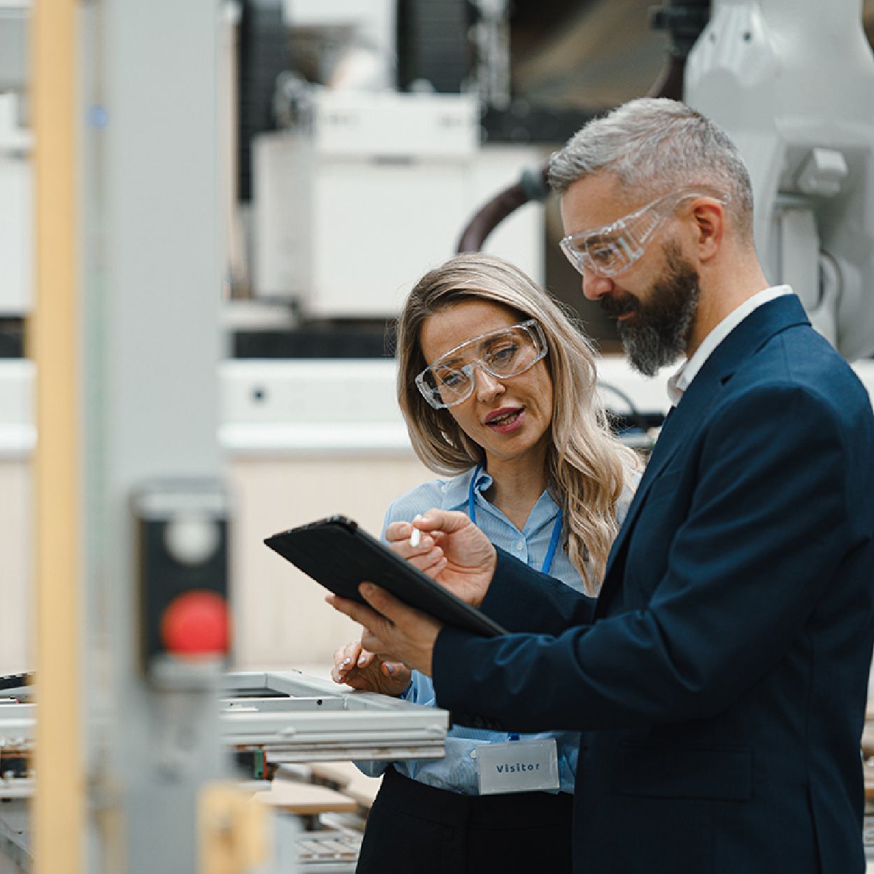 Man and woman with safety glasses review tablet in a factory setting.