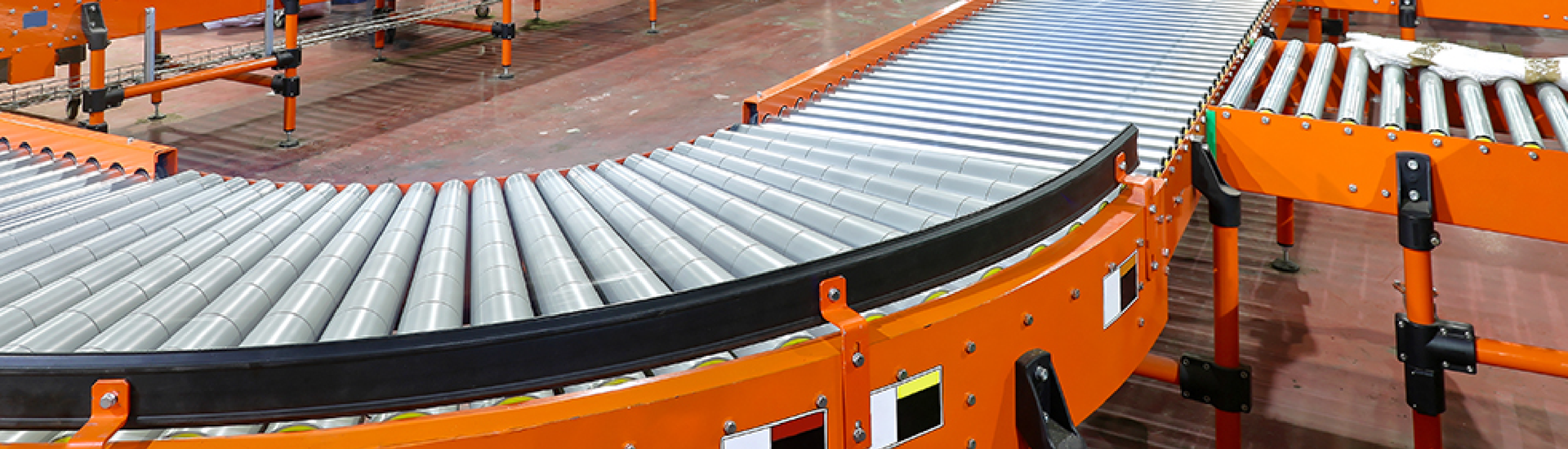 Orange conveyor line with silver rollers carrying luggage in an airport baggage sorting area