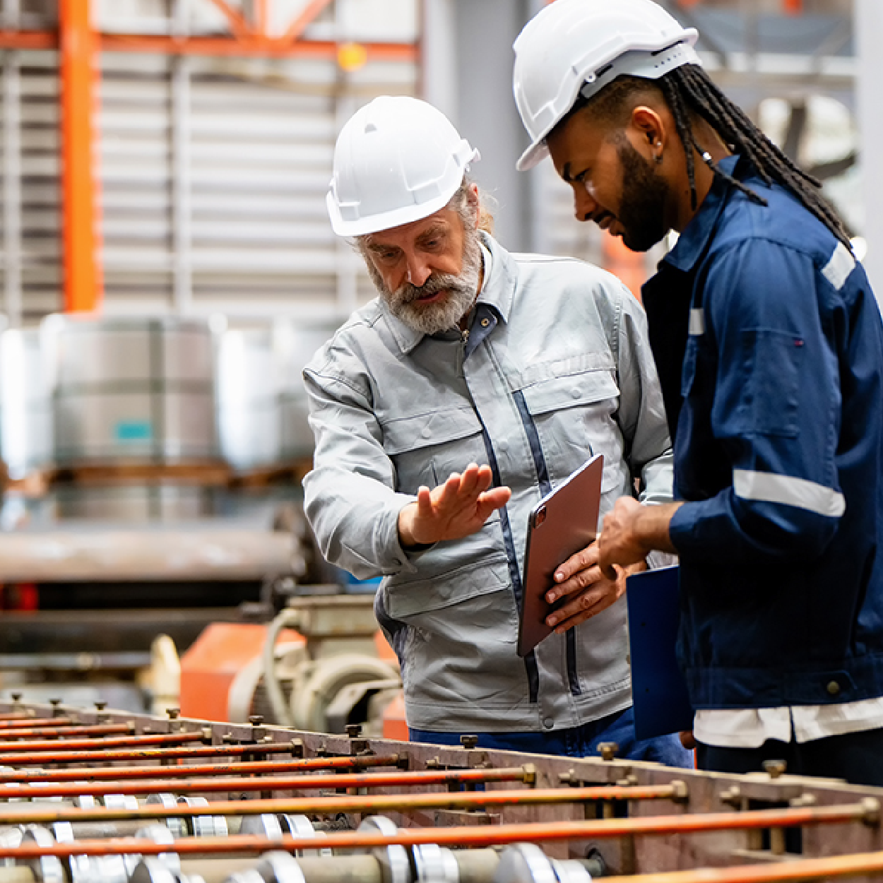Two workers in hard hats review plans beside construction materials at a worksite.