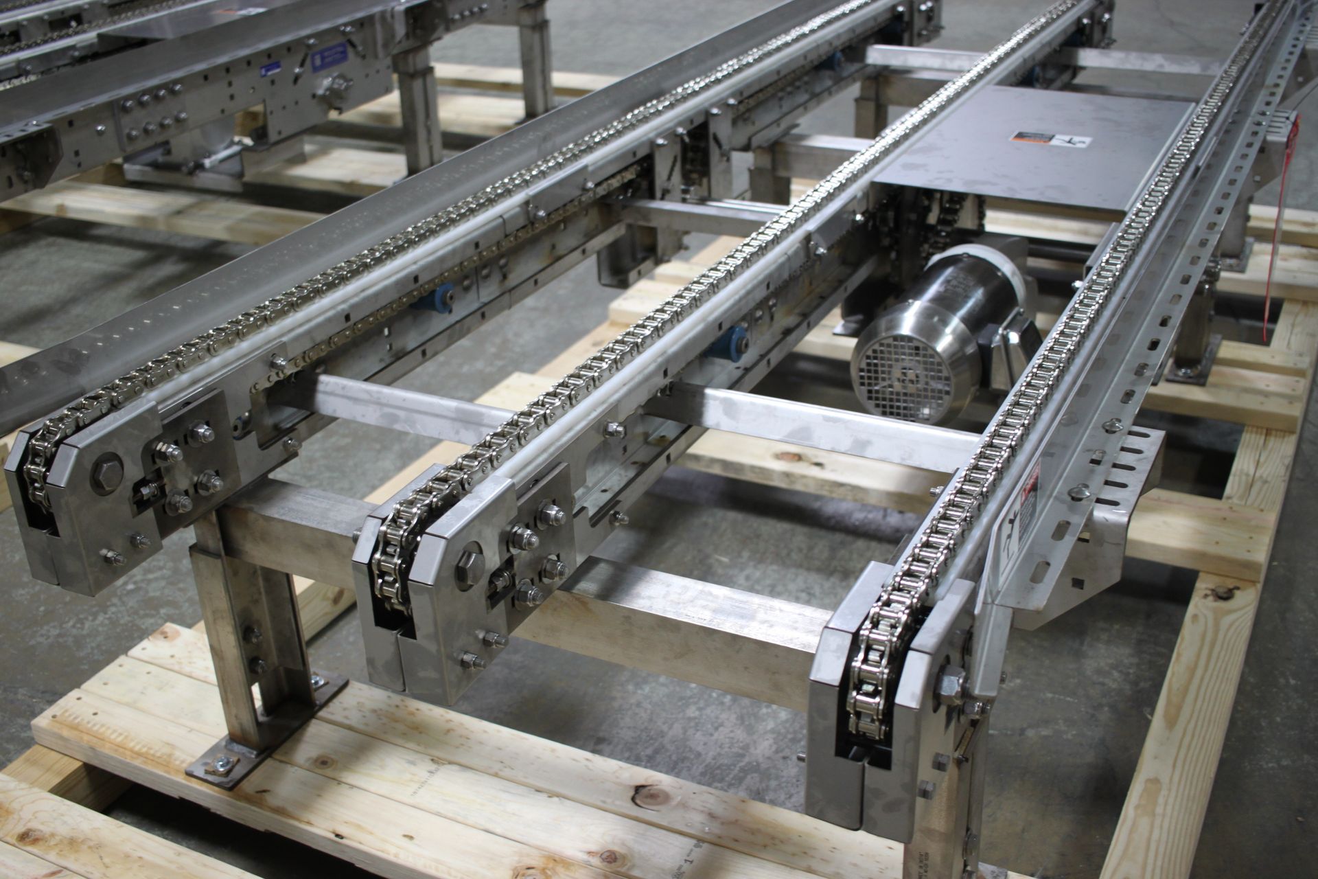 Metal conveyor rails and chains on a wooden pallet, showing industrial machinery assembly parts