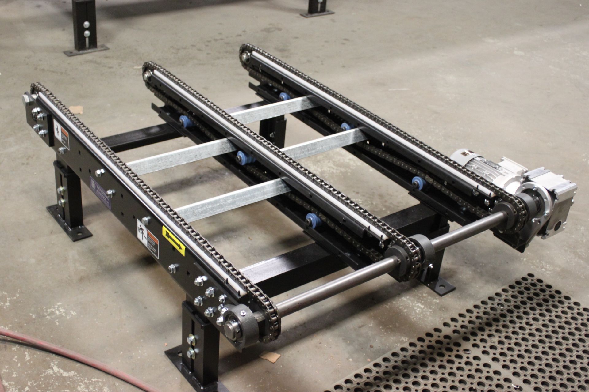 Black metal conveyor or robotic lift frame on a concrete floor, with rollers and gears.