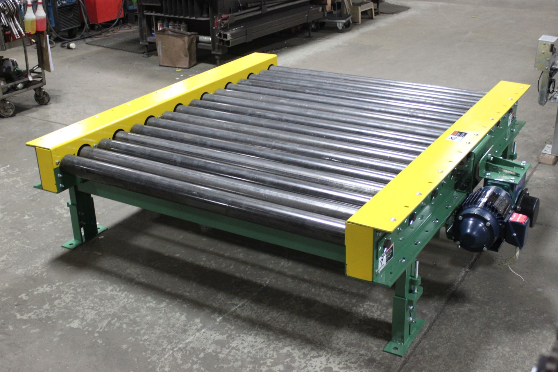 Industrial roller conveyor with yellow side rails and green frame in a workshop