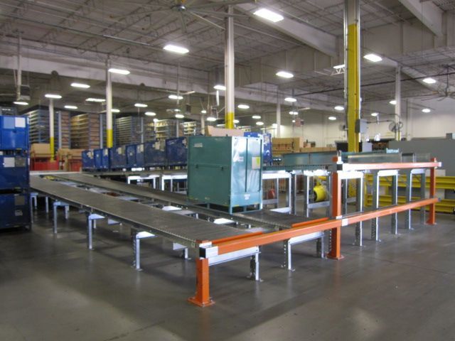 Industrial conveyor line in a warehouse with metal tables, orange safety rails, and machinery