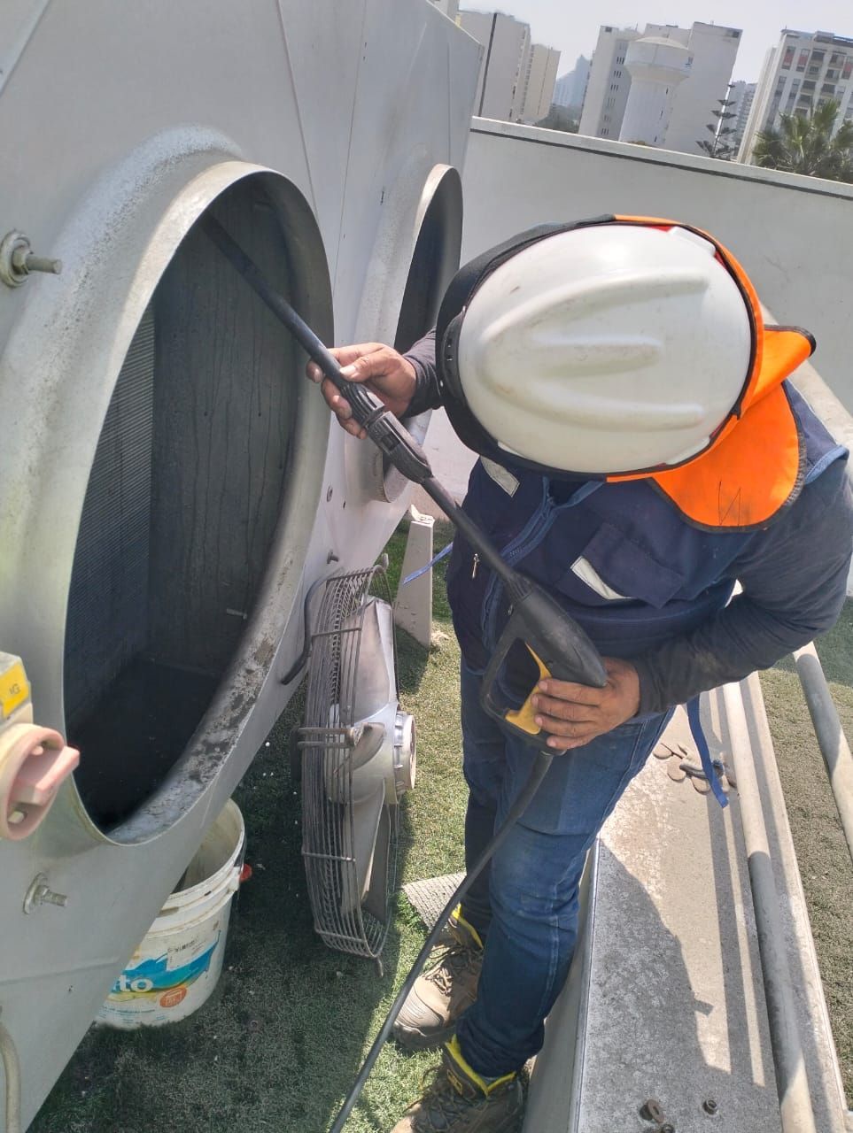 Un trabajador con casco inspecciona una gran rejilla de ventilación en el tejado con una herramienta.