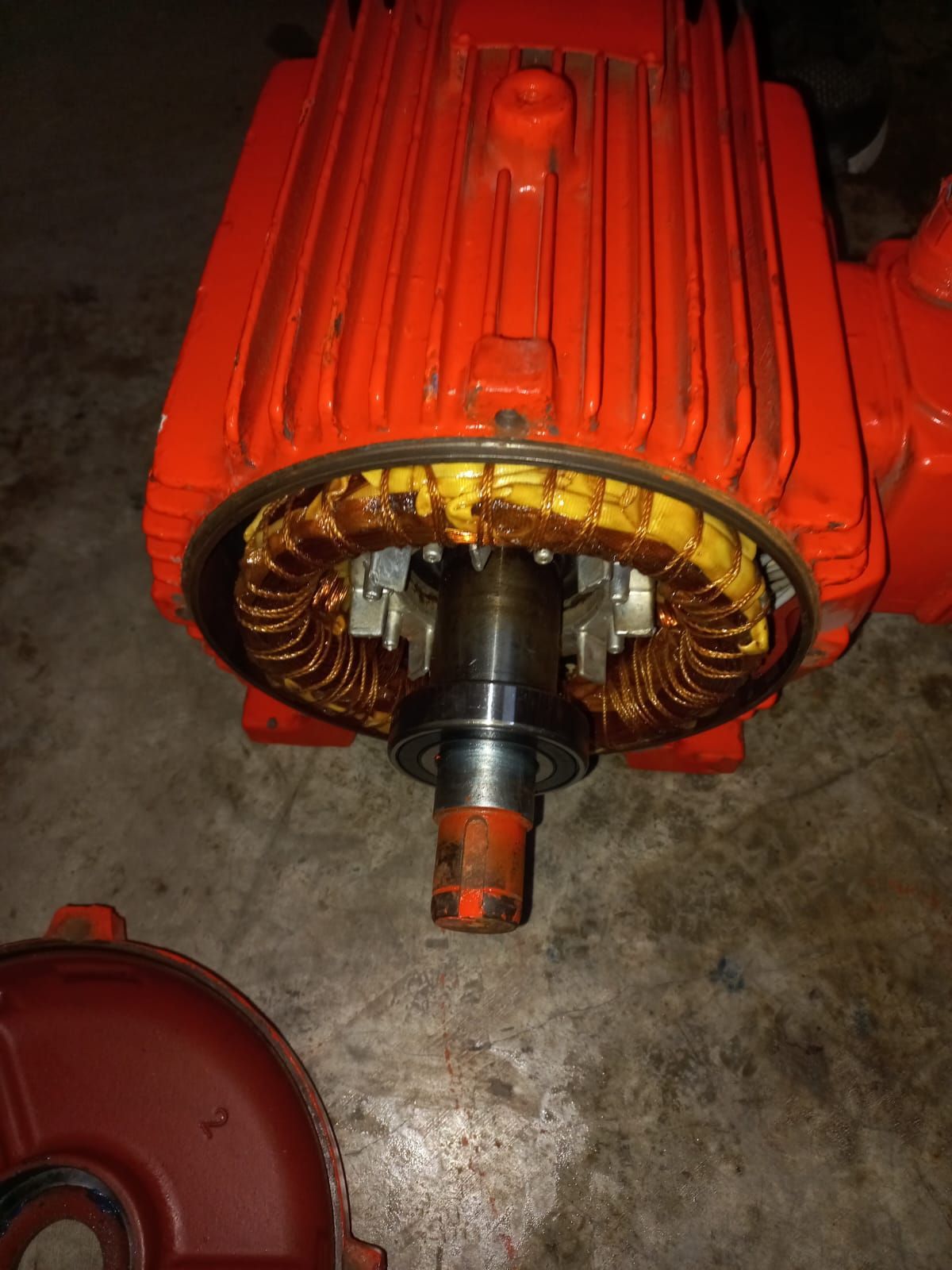 Motor eléctrico rojo con bobinados de cobre expuestos sobre un suelo de hormigón, visto desde el extremo del eje.