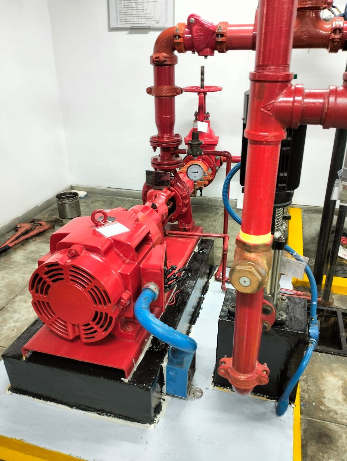 Bomba contra incendios roja y tuberías rojas en un cuarto de servicio con mangueras azules sobre una base negra.