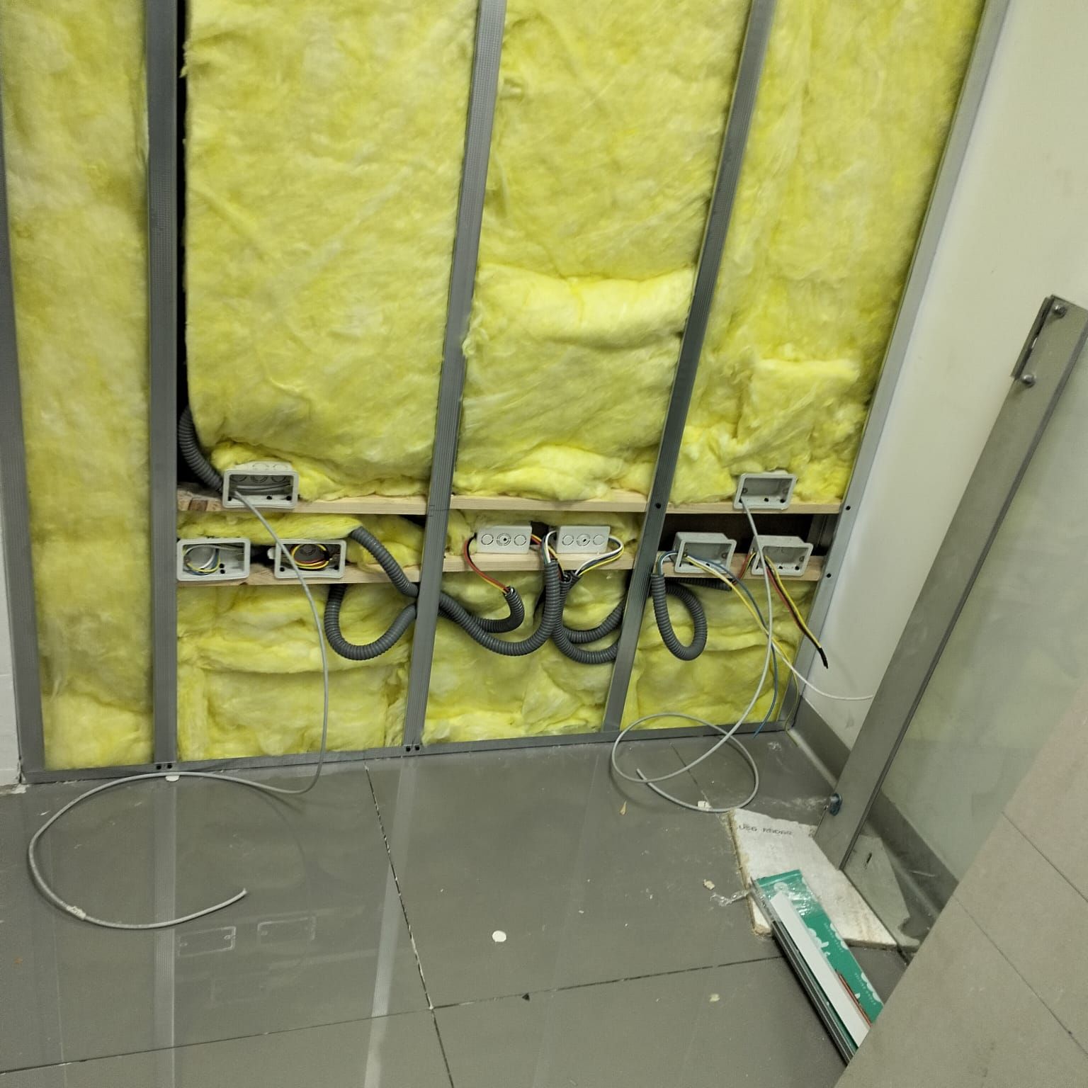Pared aislada con cableado eléctrico y enchufes expuestos, instalada sobre un suelo de baldosas.