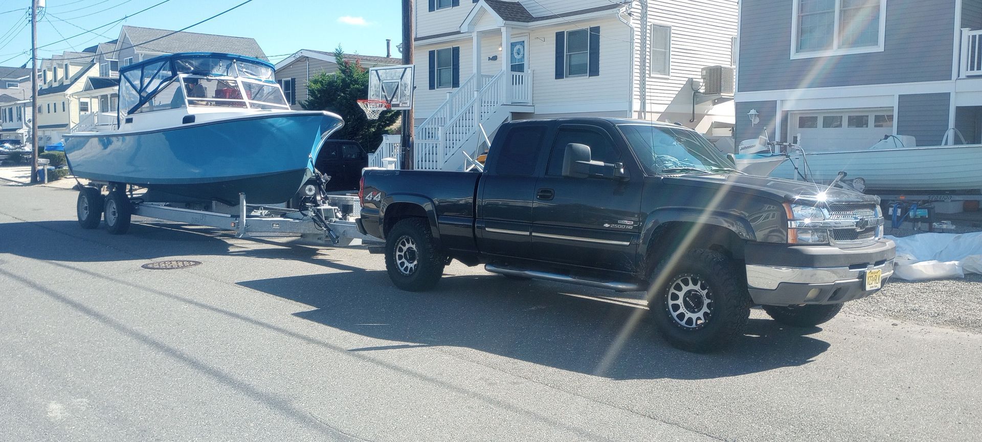 A black truck is towing a boat down a street.