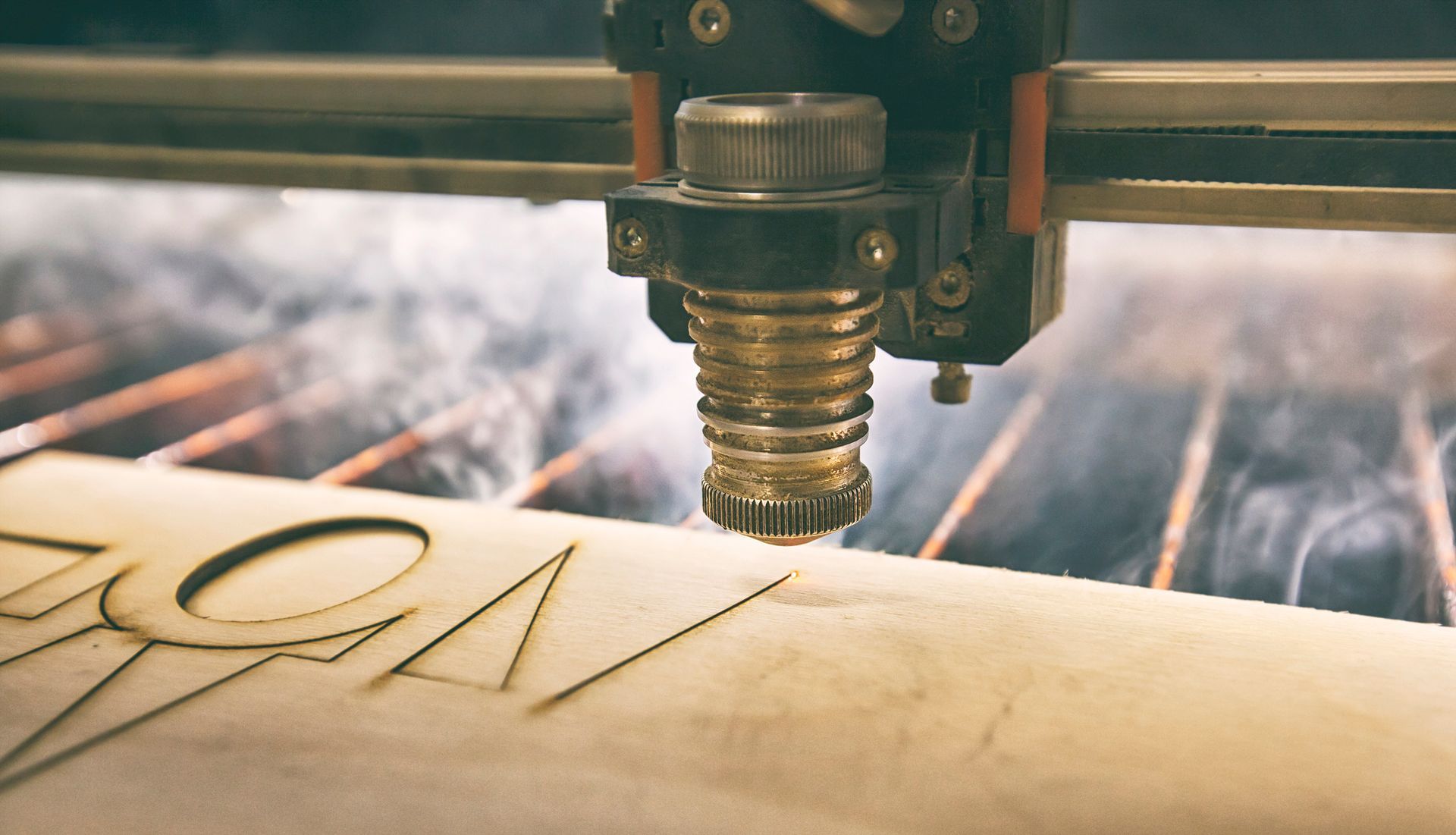 Laser cutter etching designs into light-colored wood, creating smoke.
