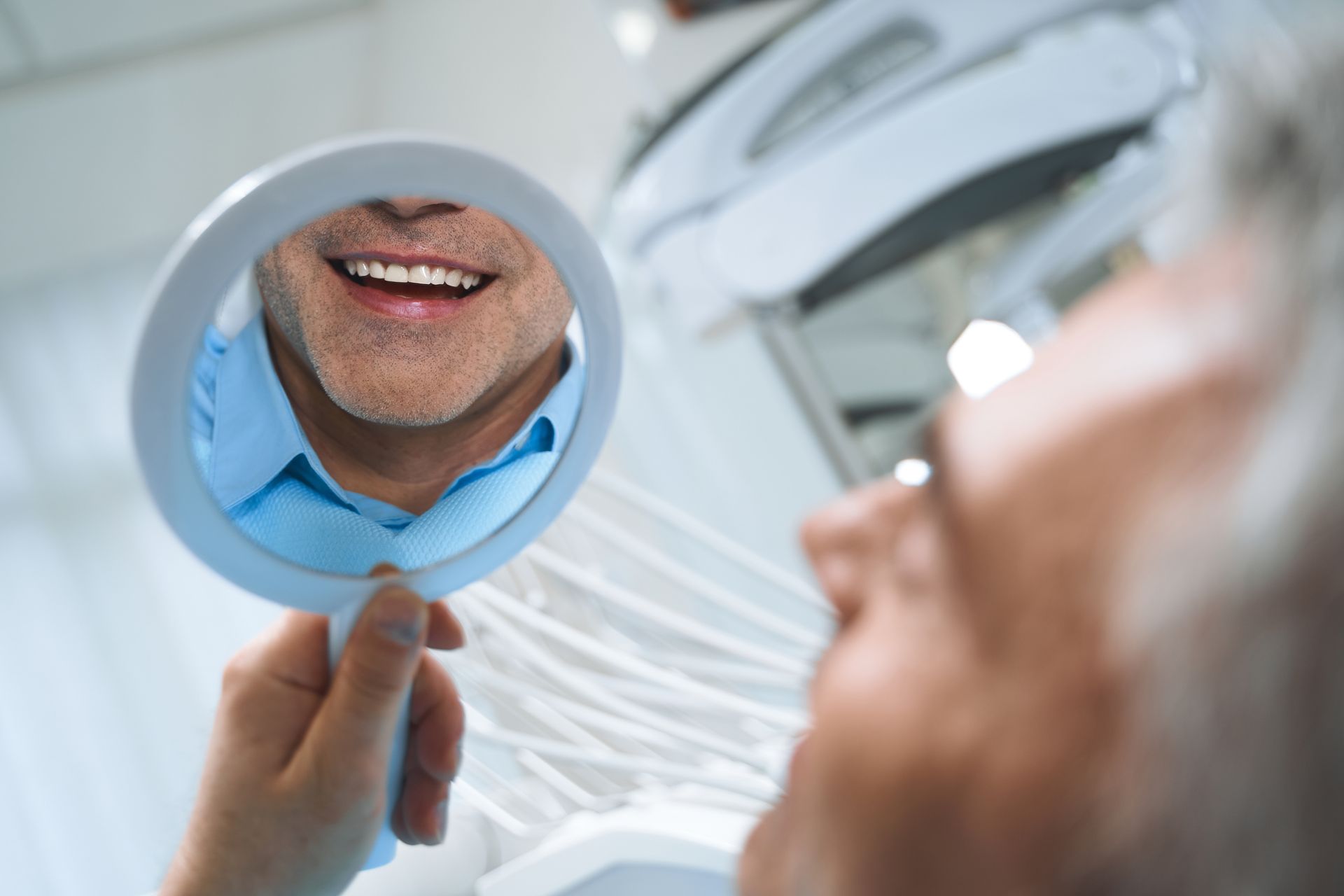 Happy man checking his smile in a mirror after getting dental implants at a modern clinic. Happy man checking his smile in a mirror after getting dental implants at a modern clinic.