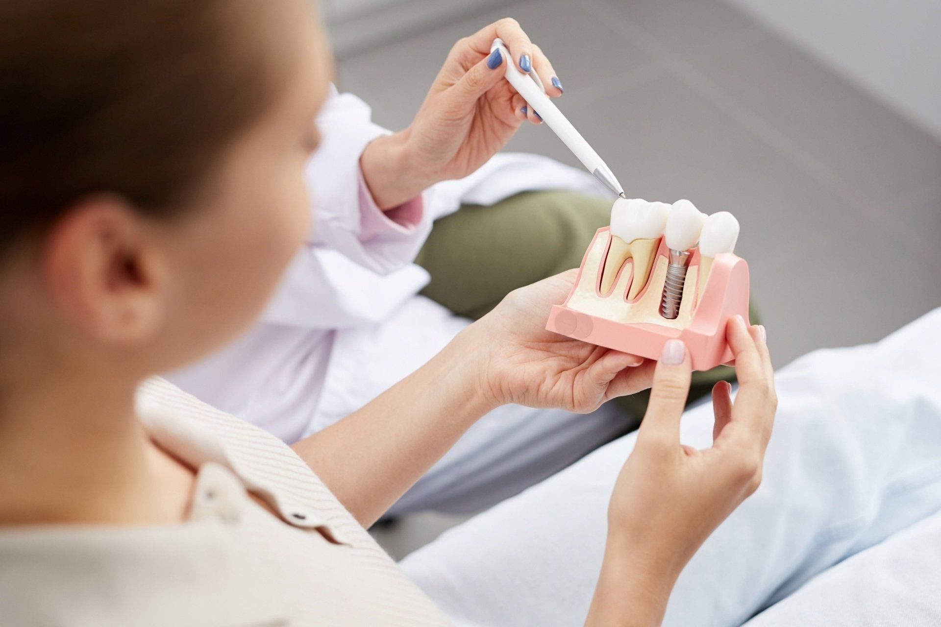 Dentist using pen to explain dental implant model to patient. Dentist using pen to explain dental implant model to patient.