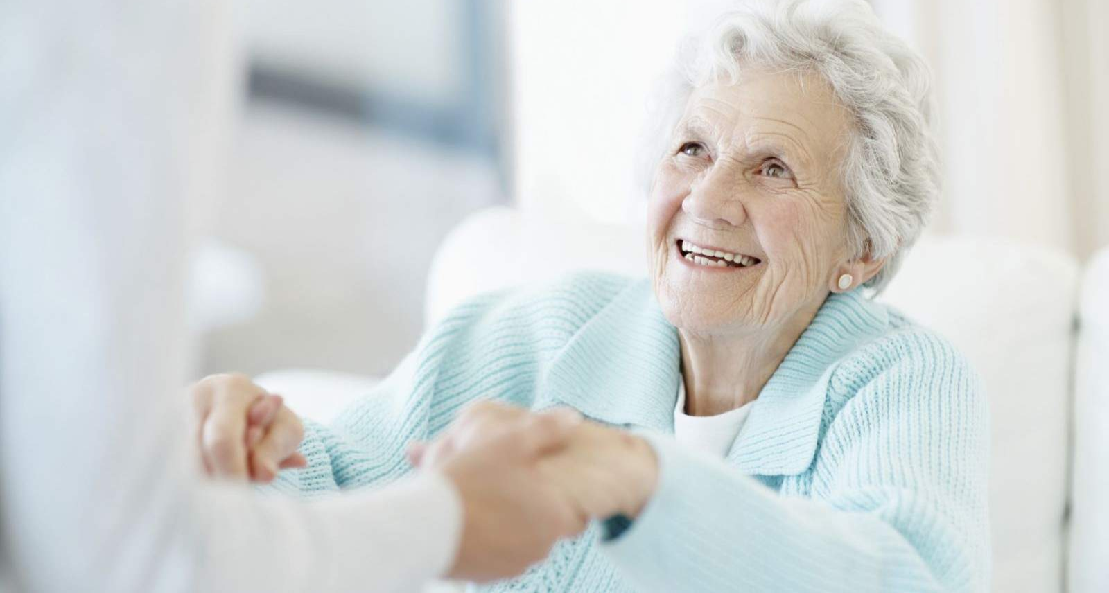 An elderly woman is holding a man 's hand and smiling.