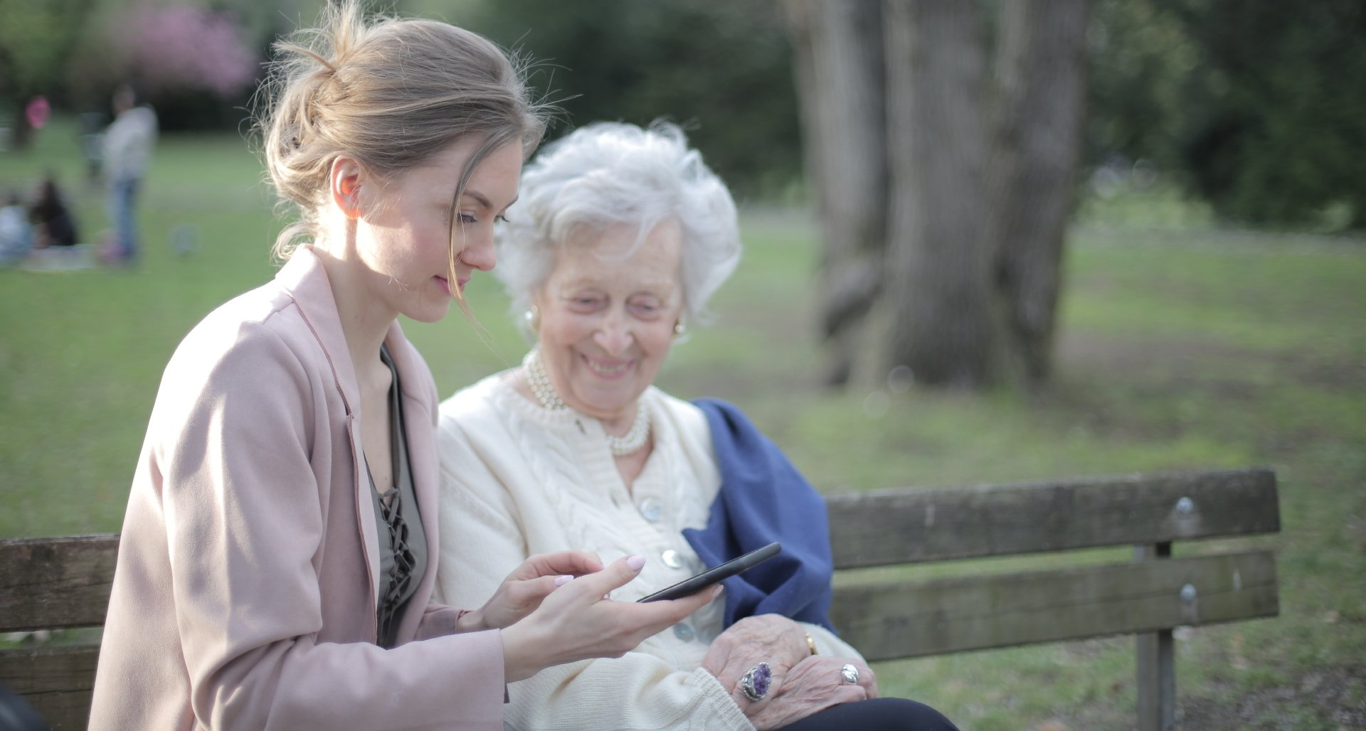 Two women are sitting on a park bench looking at a cell phone.