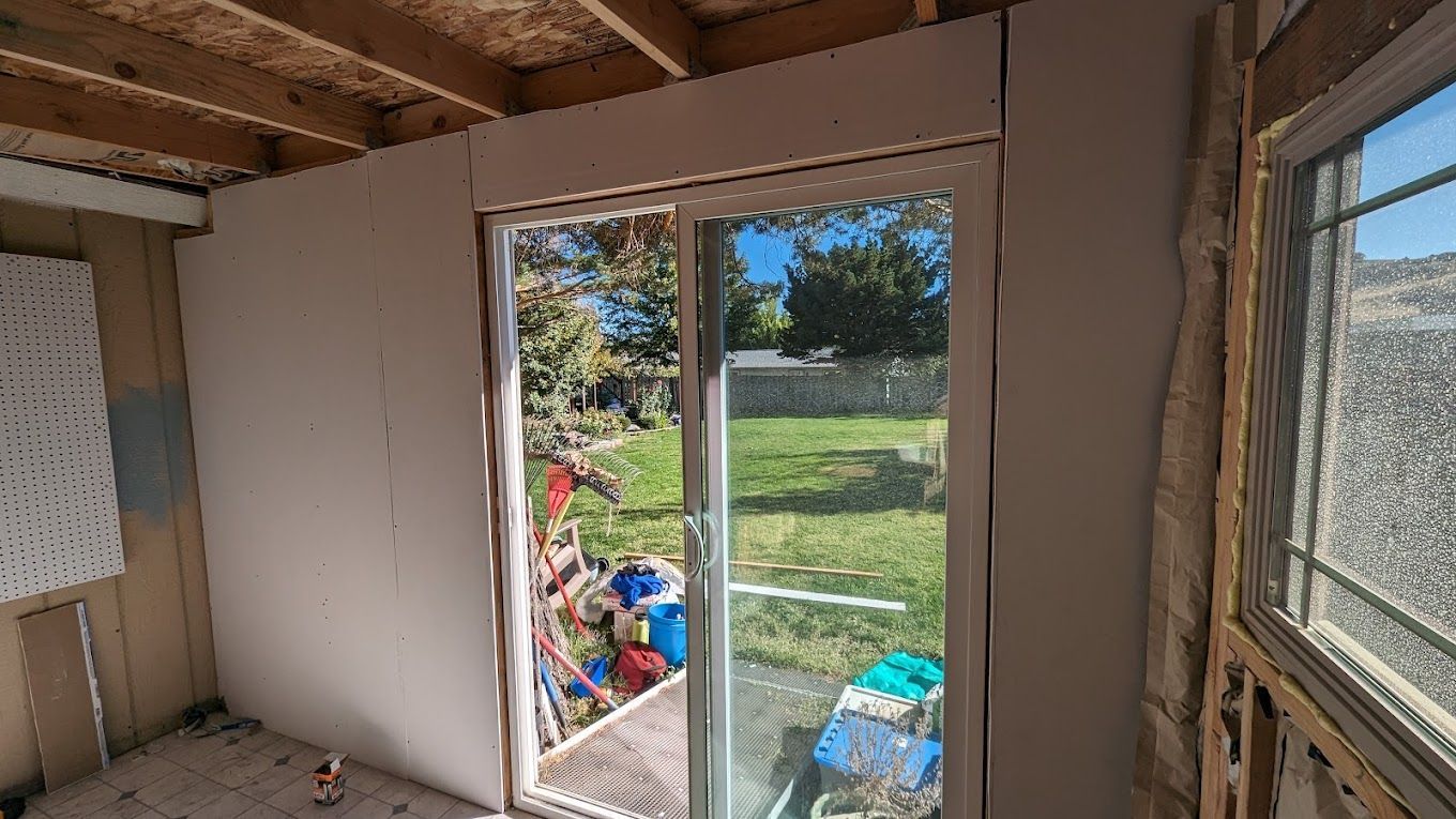 Interior view of room with new drywall around sliding glass door, looking out at a backyard.