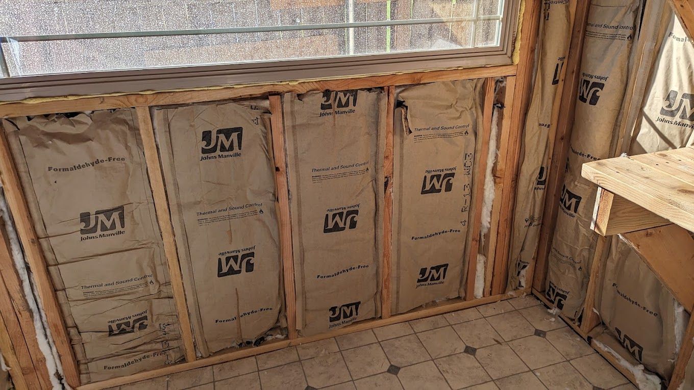 Interior wall construction, insulation installed between wooden studs. A window is visible above.