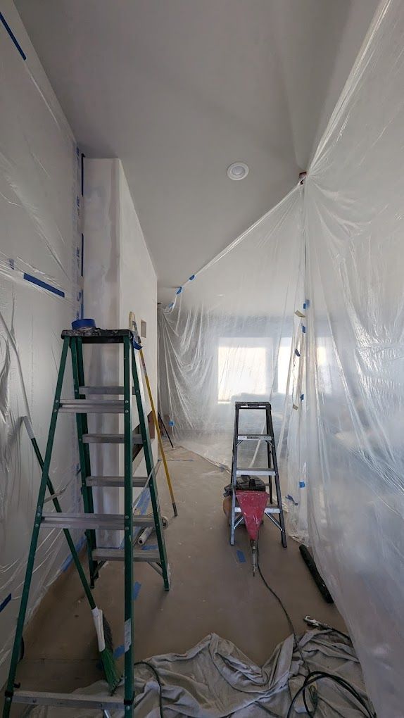 Interior room under renovation, plastic sheeting containment. Ladder, tools, and construction debris.