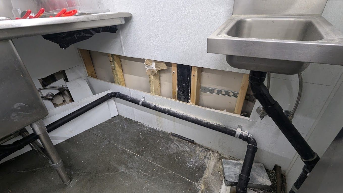 Damaged commercial kitchen wall with exposed wooden studs, sink, and plumbing.