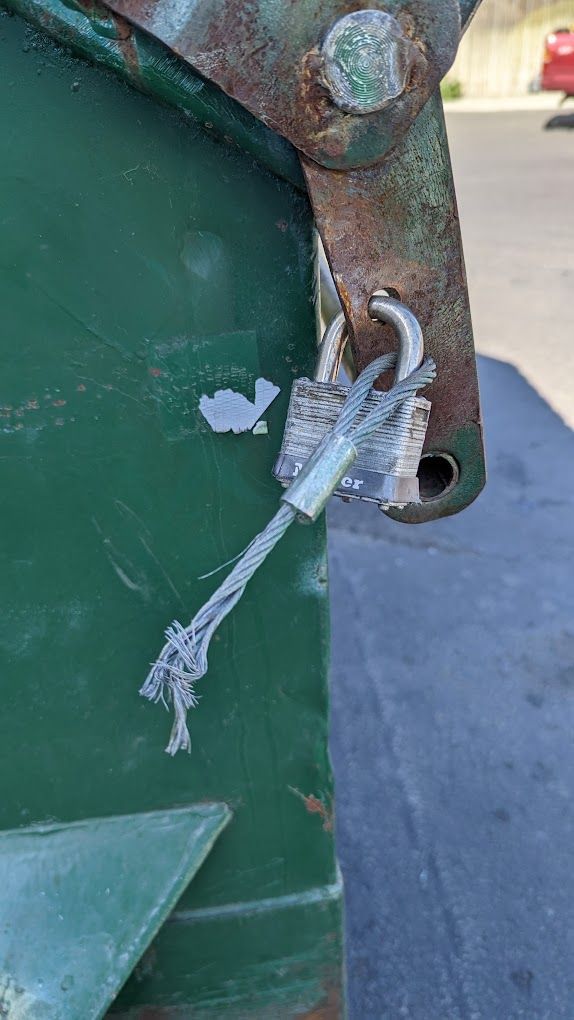 Green dumpster with torn cable locking the lid.