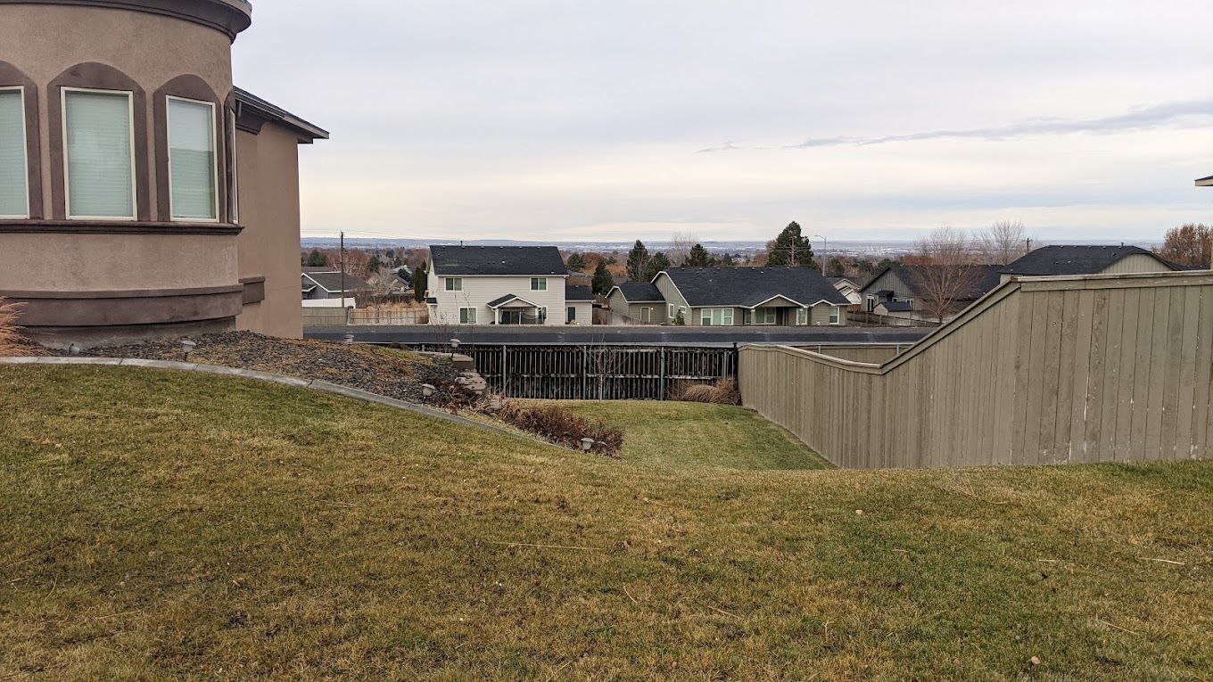 Backyard view of suburban homes under a cloudy sky, with a fenced area and grassy lawn in the foreground.