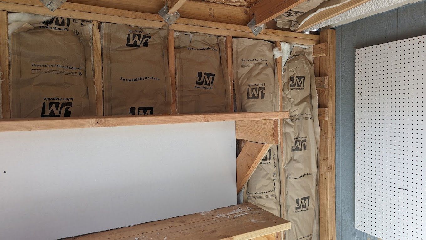 Interior wall under construction, insulation exposed between wood studs. A shelf is installed.