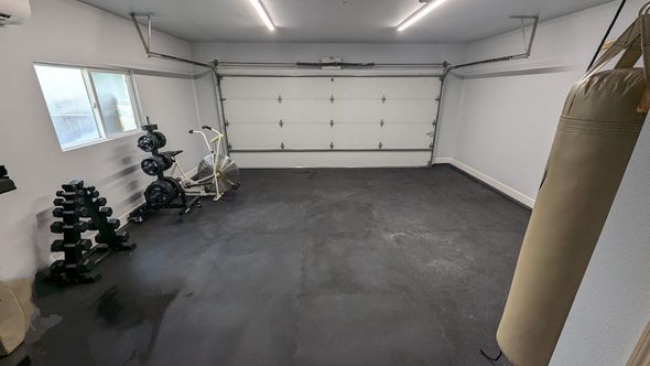 Garage gym with weights, punching bag, and exercise equipment. Dark floor, white walls and garage door.
