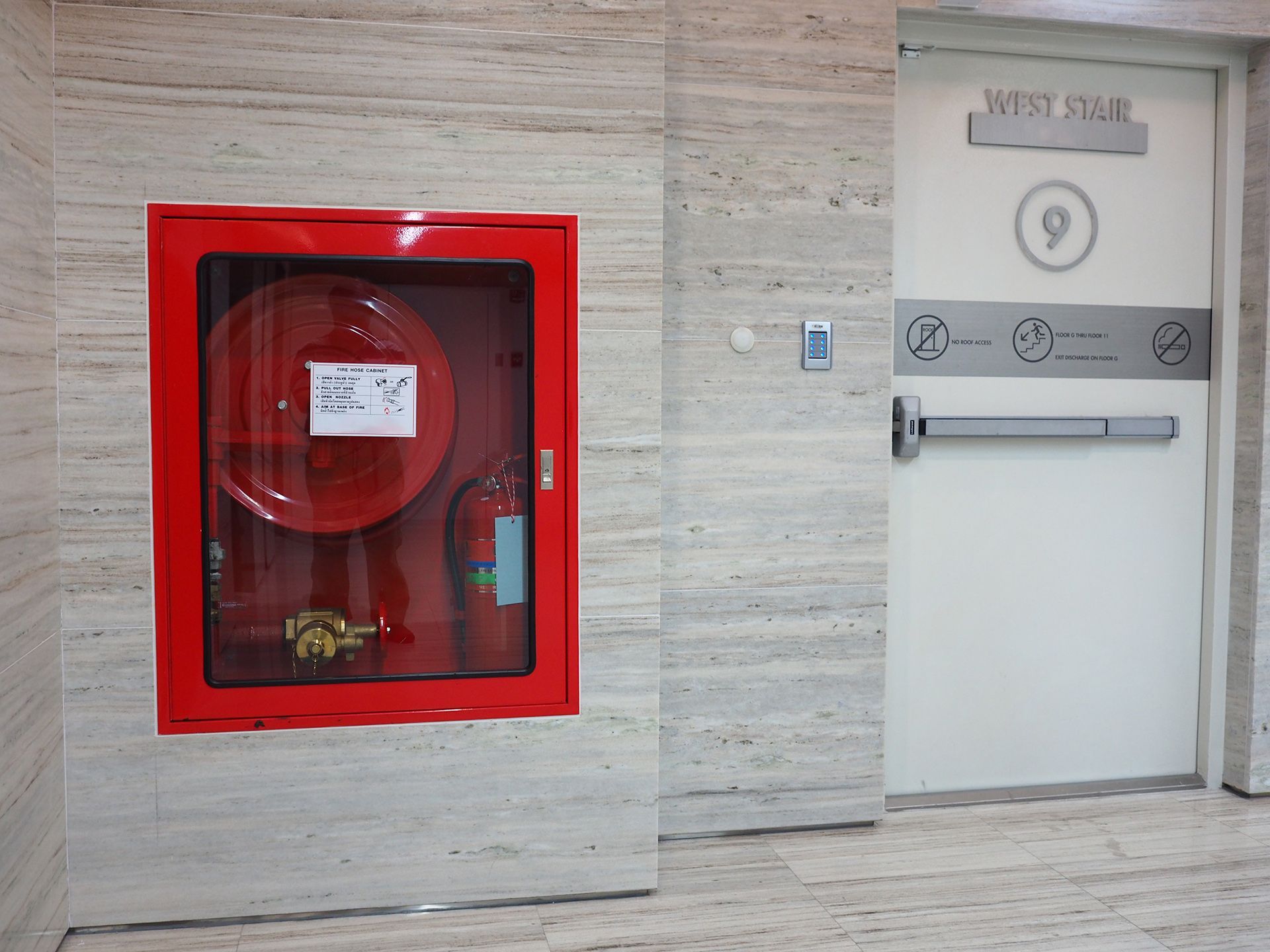 Una manguera contra incendios roja cuelga de una pared junto a una puerta blanca.