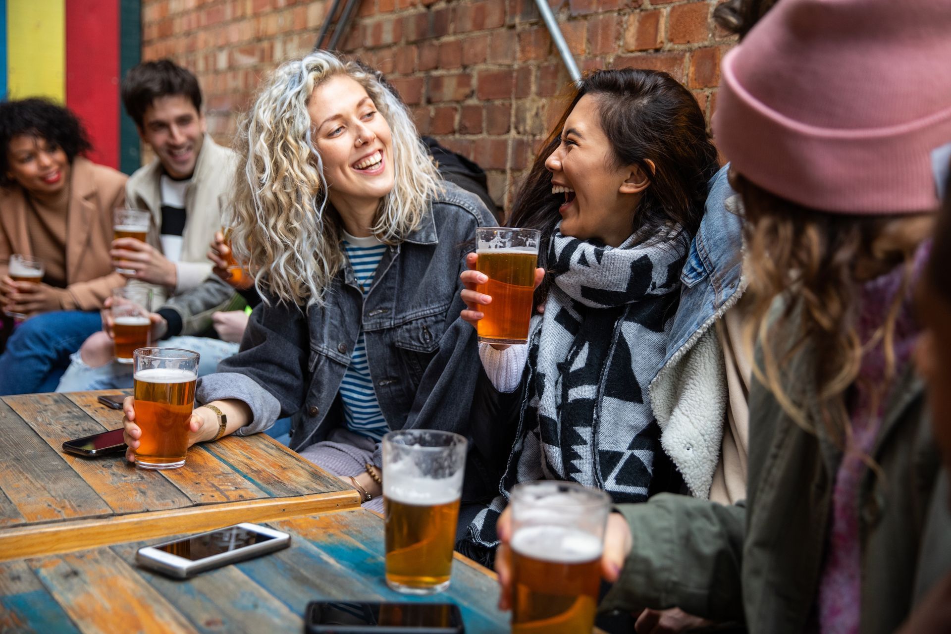 Friends laughing and enjoying drinks together at an outdoor brewery or beer garden.
