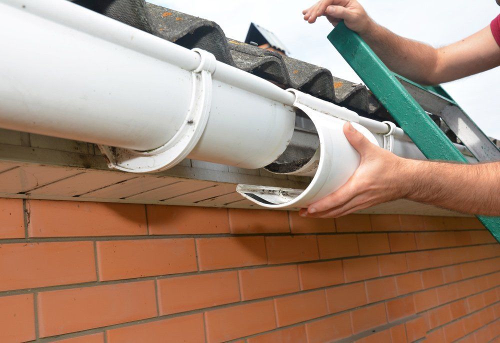 A Man Is Installing A Gutter On The Side Of A Brick Building — Malouf Plumbing In Pie Creek, QLD