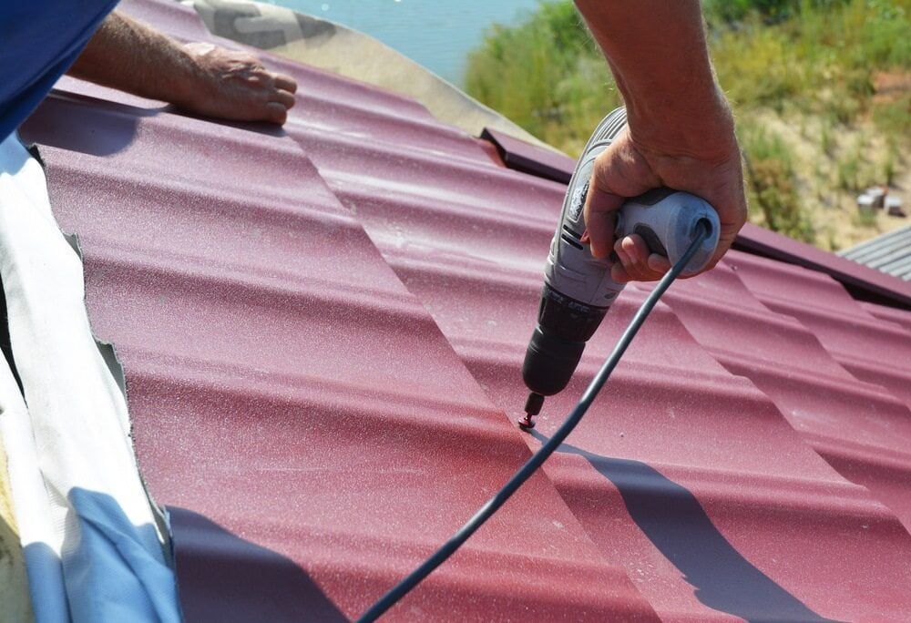 A Person Is Using A Drill On A Red Roof — Malouf Plumbing In Pie Creek, QLD
