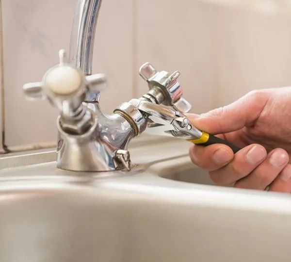 A Person Is Fixing A Sink Faucet With A Wrench — Malouf Plumbing In Pie Creek, QLD