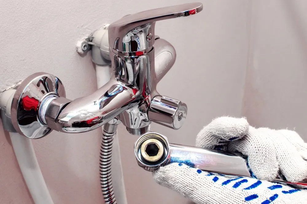 A Person Is Fixing A Bathroom Faucet With A Wrench — Malouf Plumbing In Mary Valley, QLD