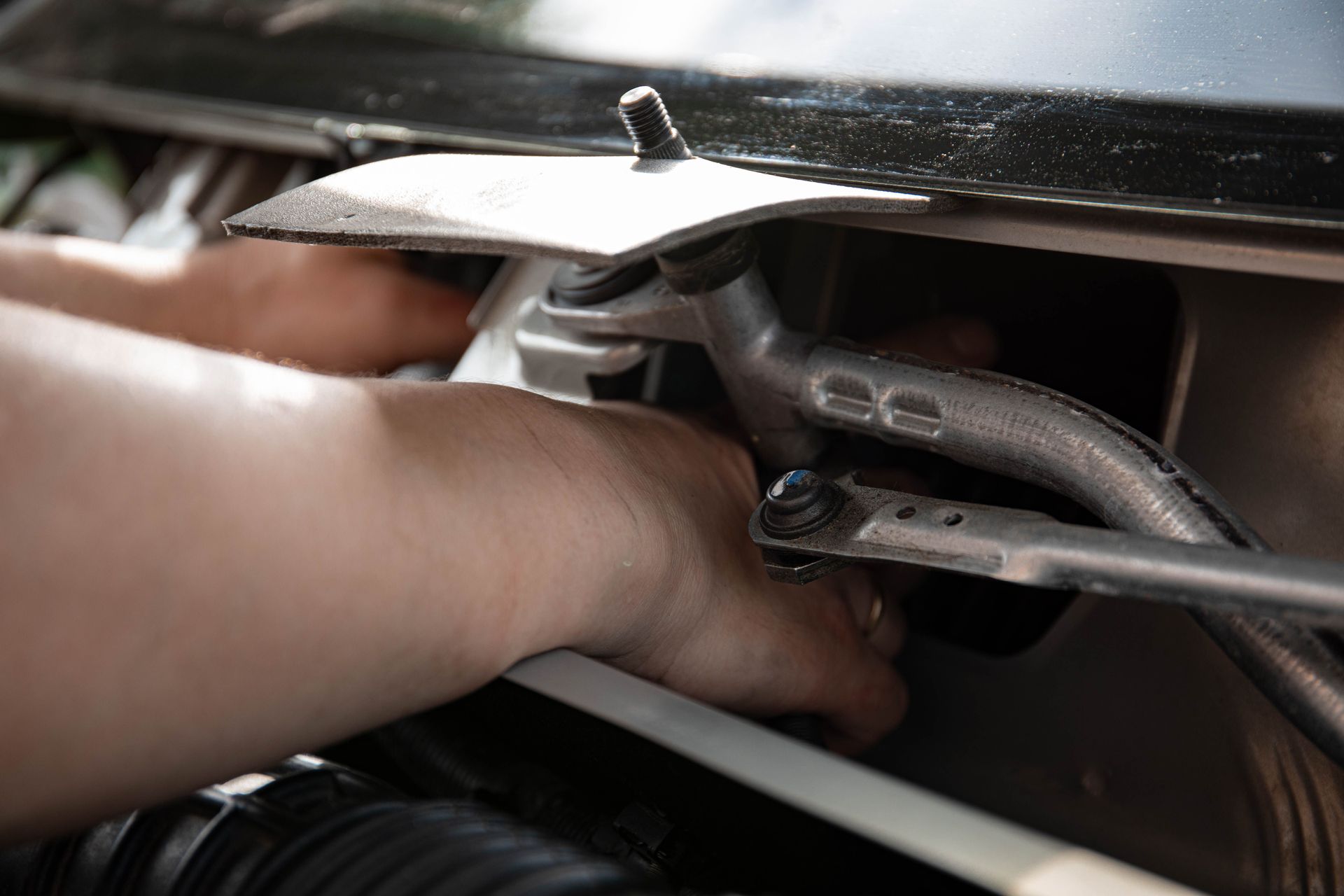 Hand tightening a clamp on a metal hose assembly under a car hood