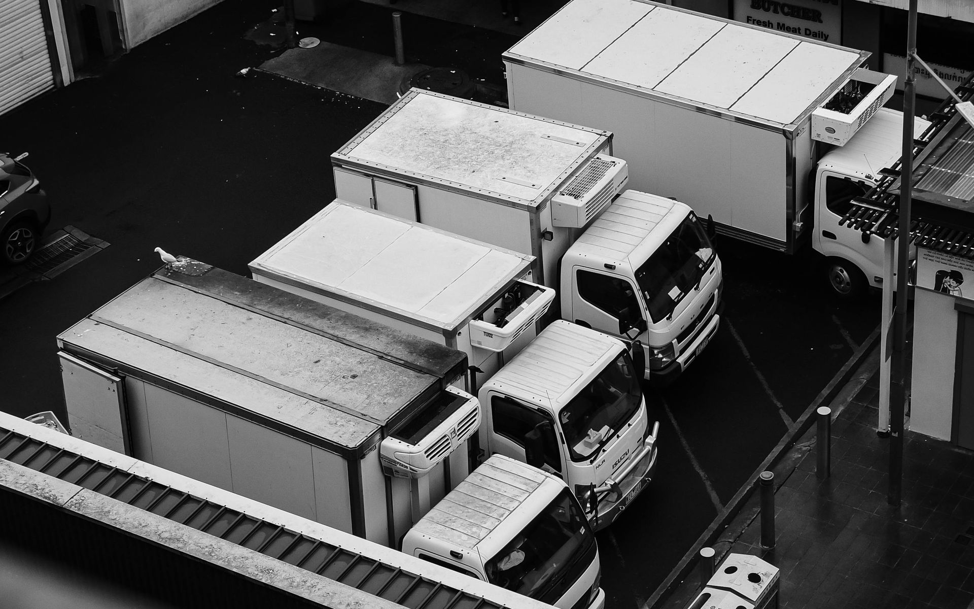 A high-angle, black-and-white view of several box trucks parked in an industrial loading area.