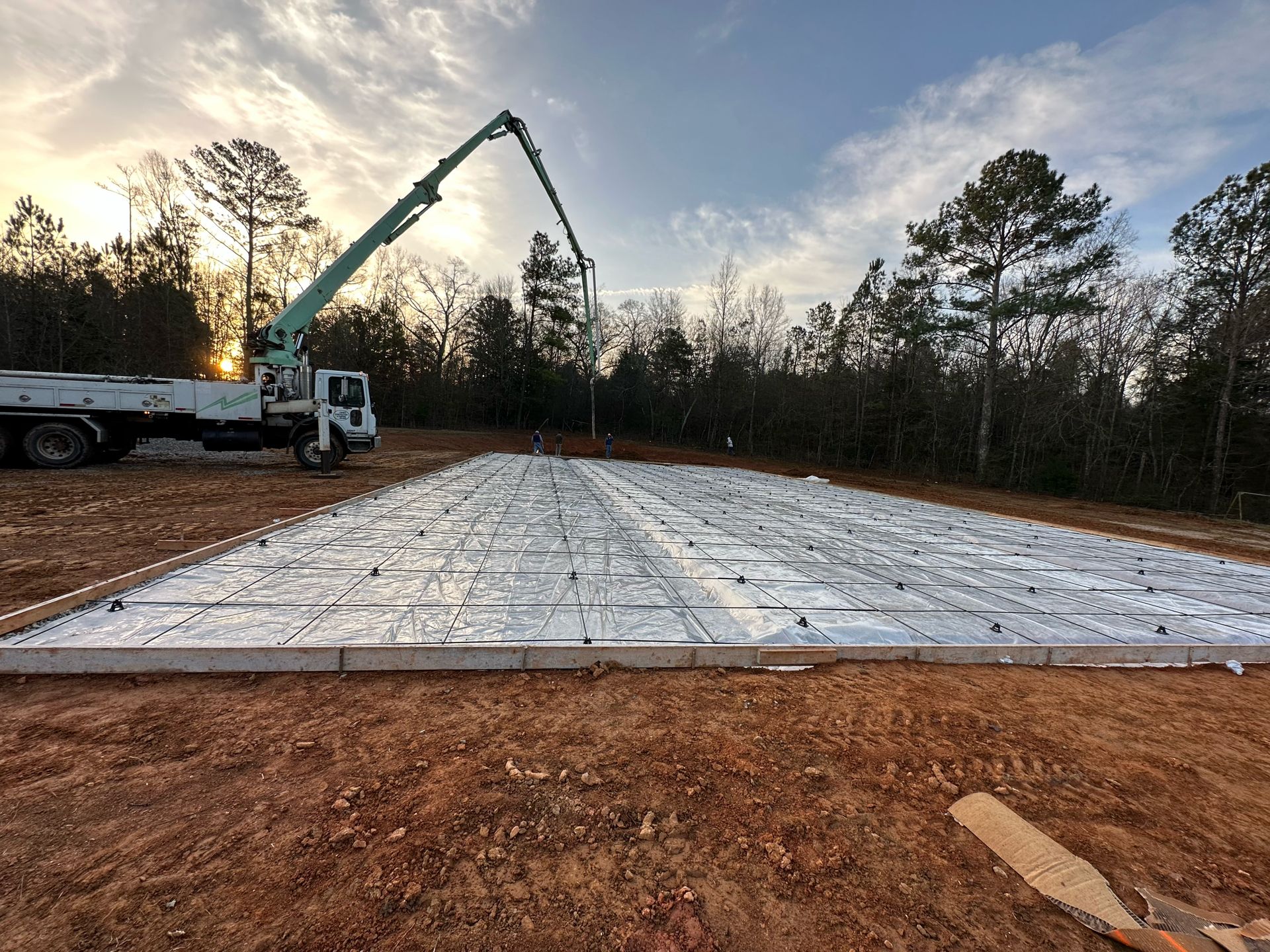 Concrete foundation slab being poured at a wooded construction site with a truck-mounted pump